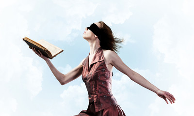 Girl against cloudy sky with opened book in palm as idea for knowledge