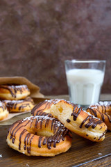 Homemade classic donuts with chocolate and coconut flakes and a glass of milk on a dark wooden background. Close up.