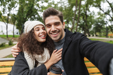 Naklejka premium Portrait of amazing couple man and woman 20s taking selfie photo, while sitting on bench in green park