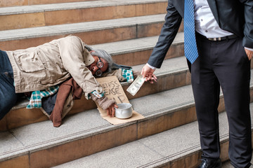 Businessman giving donation dollar cash with sleeping homeless person