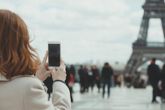 Girl takes pictures of a Eiffel Tower on a smartphone