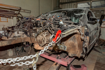 A broken car with a violation of geometry is on the stocks for leveling and repair in the workshop and auto service for the restoration of vehicles on building berth with chain and red hook
