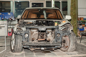 Disassembled white car in the workshop prepared for repair: front end, hood and bumper removed, internal equipment, parts and spare parts visible, without engine.