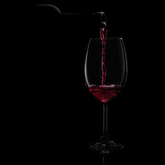 Pouring red wine into a glass on a black background. Close-up studio shot.