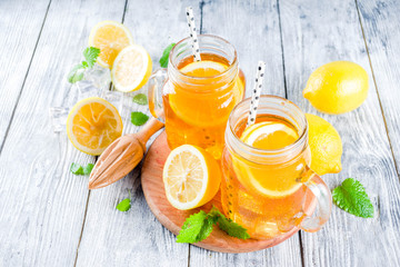 Iced summer drink, tea with lemon slices and mint, rustic wooden background copy space