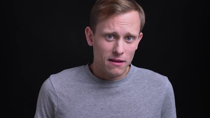 Closeup portrait of young attractive caucasian man looking at camera and awkwardly smiling with background isolated on black