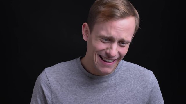 Closeup portrait of young attractive caucasian man looking at camera and awkwardly smiling with background isolated on black