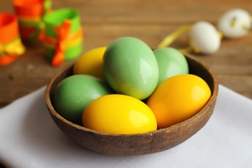 Colorful easter eggs in a brown blow on a white napkin. Wooden background, horizontal orientation