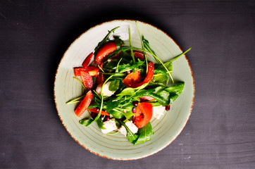 Fresh spring salad with rucola, feta cheese, red onion and pomegranate seeds in black bowl on chalkboard background.