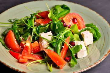 Fresh spring salad with rucola, feta cheese, red onion and pomegranate seeds in black bowl on chalkboard background.