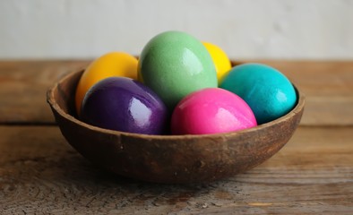 Fototapeta na wymiar Colorful easter eggs in a brown bowl. Wooden table, light backgroun, close up