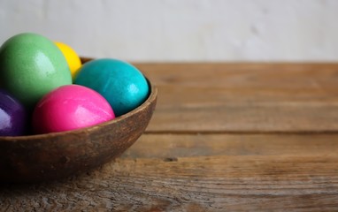 Colorful easter eggs in a brown bowl. Wooden table, light background. Copy space, horizontal orientation