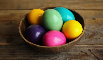 Fototapeta na wymiar Colorful easter eggs in a brown bowl on a wooden background. Close up, horizontal orientation
