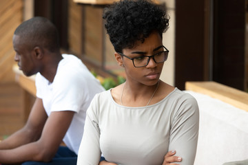 Black unhappy couple sitting on sofa separately at each other