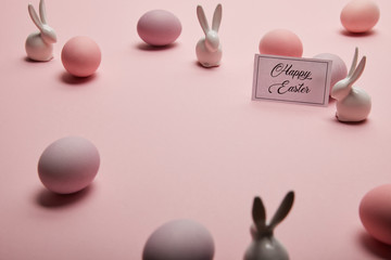 toy bunnies, card with happy easter lettering and easter eggs on pink background with copy space