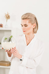 beautiful woman looking at glass fish bowl with sand and green small leaves,  environmental saving concept