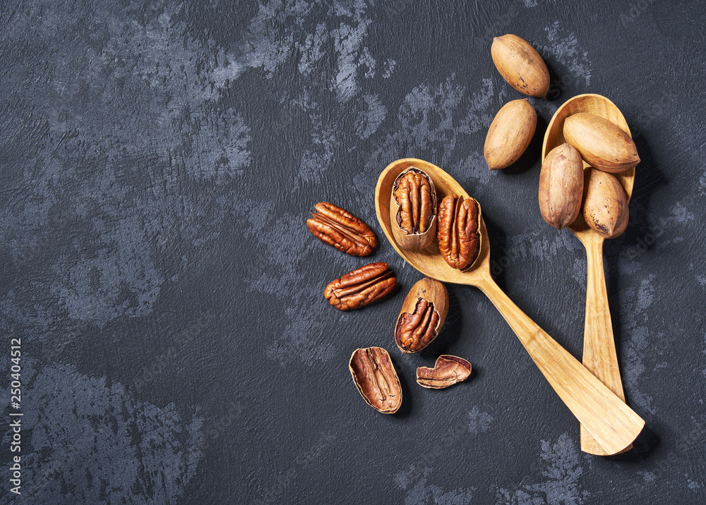 Wall mural pecan in two wooden spoons on black table ,with copy space ,top view