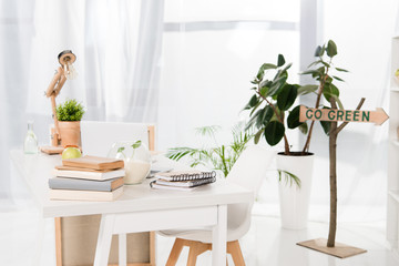 workspace with books and laptop near go green sign in modern office, environmental saving concept