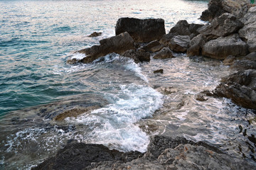 Wild sea panorama surrounded with sharp rock stones in summer on sunny sunset day. Beauty and force of deep water. Danger o swimming in forbidden places.