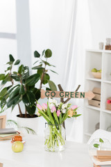 selective focus of flowers in glass vase near wooden sign with go green lettering on background, environmental saving concept
