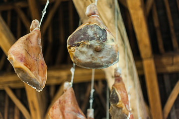 Hooked ham on wooden beams that hang from the ceiling. Traditional way of drying meat. Pork ham drying on the air