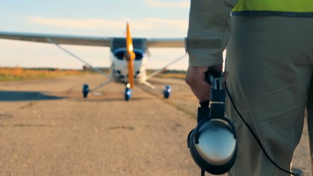 A person holds headphones while walking on a runway, back view.