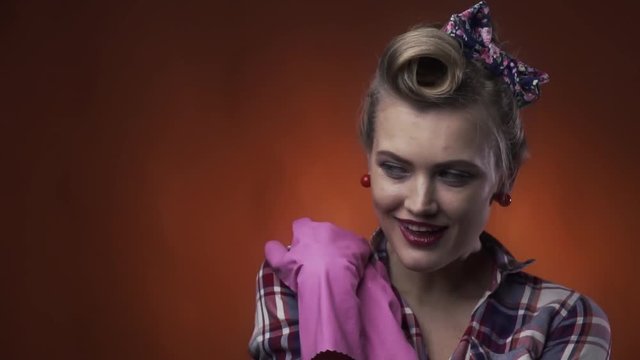 Blonde sexy pin up girl is wearing pink rubber gloves and wiping the sweat off her forehead with the smile on her face