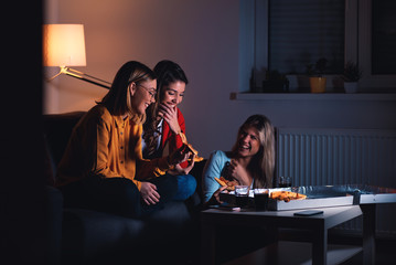 Three female friends chatting and enjoying eating pizza at home.