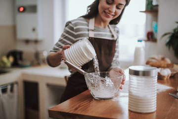 Cheerful woman is kneading dough in kitchen
