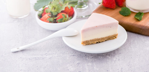 Delicious and nutritious handmade strawberry no bake frozen gradient colour fromage frais cheesecake slice with raw sarcocarp besides isolated with fair-faced gray background, copy space, close up