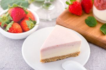 Delicious and nutritious handmade strawberry no bake frozen gradient colour fromage frais cheesecake slice with raw sarcocarp besides isolated with fair-faced gray background, copy space, close up