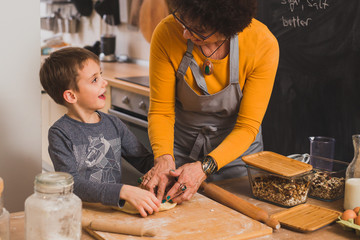 teaching her grandson making pizza dough in kitchen
