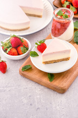 Delicious and nutritious handmade strawberry no bake frozen gradient colour fromage frais cheesecake slice with raw sarcocarp besides isolated with fair-faced gray background, copy space, close up