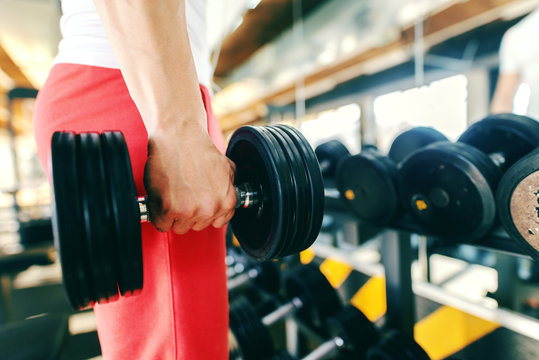 Close up of man picking dumbbell while standing in the gym.