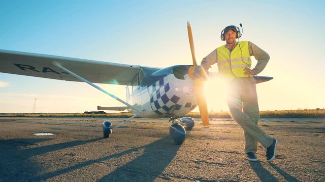 Aviator stands near an airplane on a susnet background, close up.