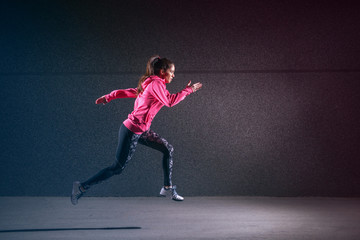 Sporty strong sporty woman running against black wall.