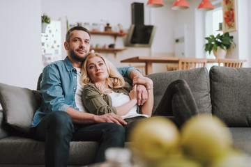 Beautiful couple sitting on comfortable couch and watching TV at home