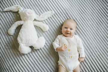 Charming little baby-girl dressed in yellow lies in grey bed