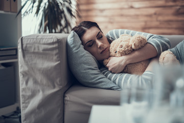 Fototapeta premium Brunette Caucasian sleepy woman lying on sofa with toy in arms