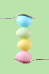 Female hand holds a spoon on which multi-colored eggs are balanced, on a green background. Unusual design, Easter concept, copy space.