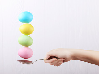 Female hand holds a spoon on which multi-colored eggs are balanced, on a white background. Unusual design, Easter concept, copy space.