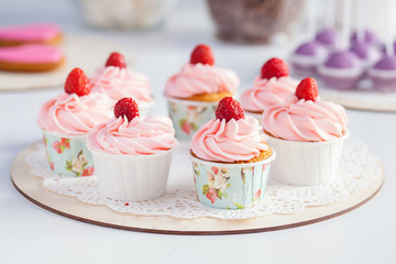 cupcakes with pink cream and raspberries on a wooden plate