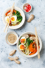 Ramen traditional japanese noodle soup with eggs, pak choi cabbage, meat broth, carrot, mushrooms in bowl on light grey background. Asian style food.
