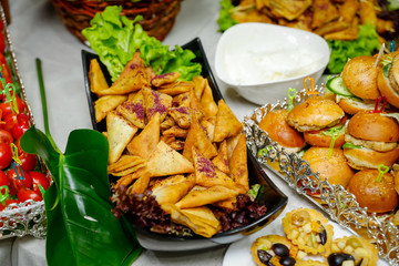 Buffet table with mini burgers, appetizers, vegetables and snacks.
