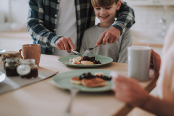 Happy kid watching his father cutting pancakes