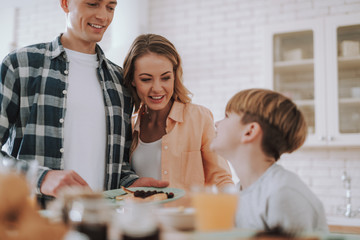 Man and woman smiling while offering pancakes to their son