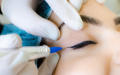 Naklejka premium Trwały tatuaż do makijażu. Kosmetolog nakładający eyeliner do makijażu permanentnego, procedura tatuażu eyeliner na młodej kobiecie w gabinecie kosmetycznym, ekstremalne zbliżenie