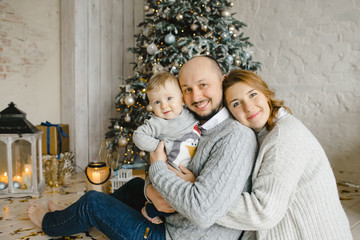 Christmas family portrait. Charming man, woman and their little son have fun posing before a Christmas tree in a bright room