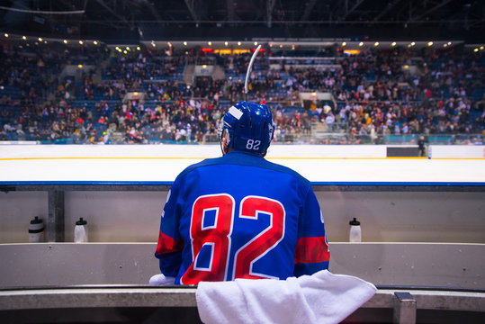 hockey player sitting on the bench, stadium and crowd in background