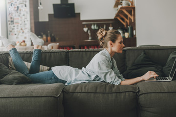 Obraz premium Happy woman laying on couch with laptop